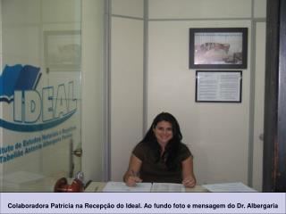 Colaboradora Patrícia na Recepção do Ideal. Ao fundo foto e mensagem do Dr. Albergaria